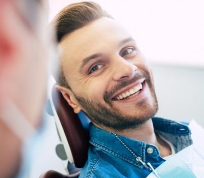 Smiling man in denim shirt leaning back in dental chair