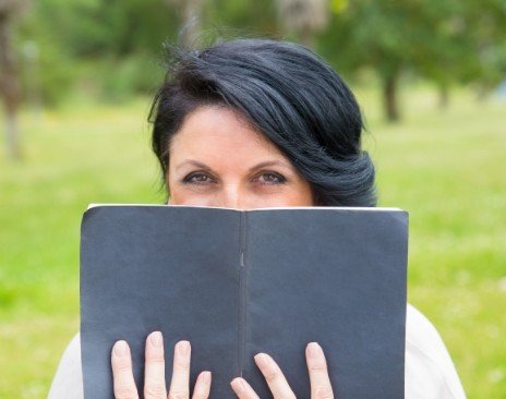Woman outdoors holding a book in front of her smile