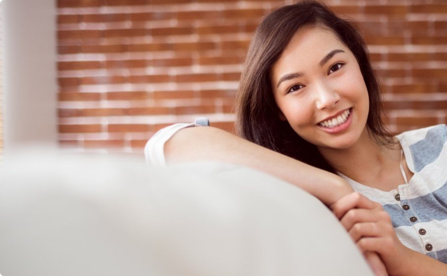 Young woman sitting on white couch and smiling after cosmetic dentistry in Hillsboro