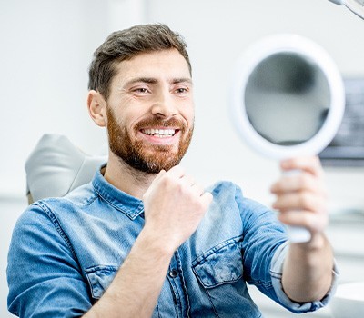 Man in dental chair looking at smile in mirror