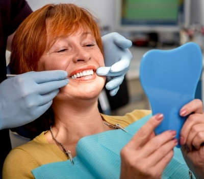 Woman with red hair in dental chair admiring her smile in mirror