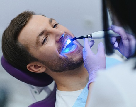 Dentist applying UV light to man’s filling