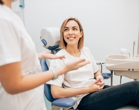 Woman in dental chair smiling while her dentist talks