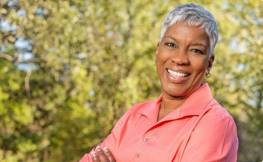 Woman in salmon colored blouse smiling outdoors after full mouth reconstruction in Hillsboro