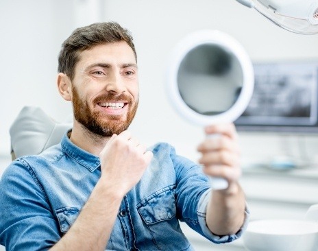 Man in dental chair looking at his smile in mirror