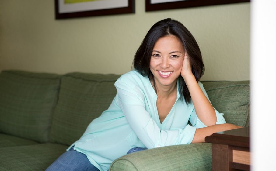 Woman sitting on couch and smiling after replacing missing teeth in Hillsboro