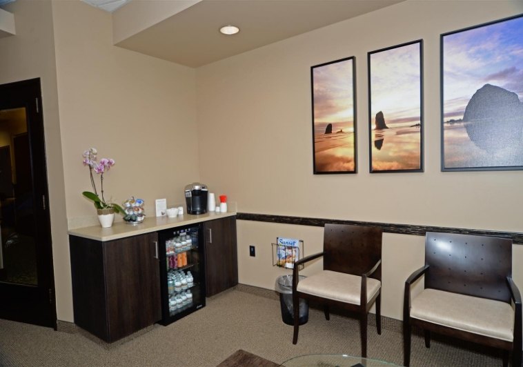 Beverage fridge next to row of chairs and paintings on wall