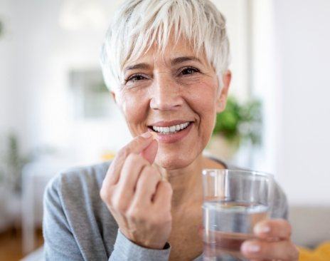 Senior woman holding pill and glass of water