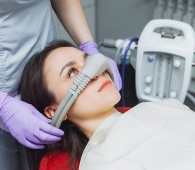 Dentist placing nitrous oxide mask on face of woman in dental chair