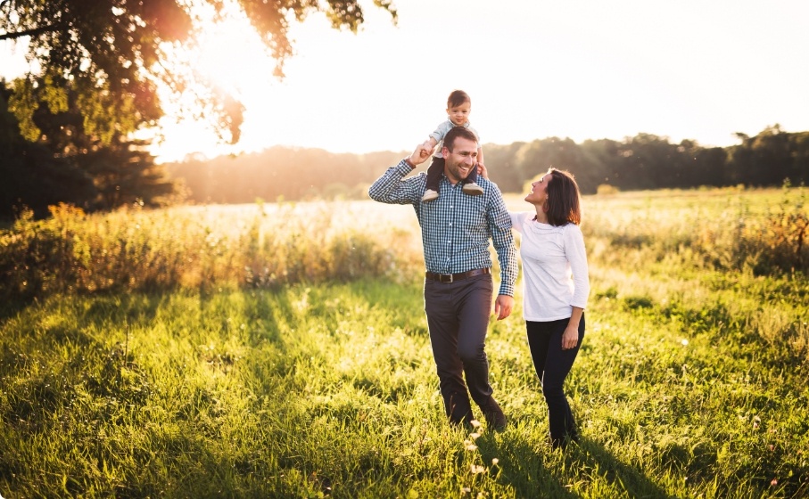 Mother and father walking in grass with their young child on sunny afternoon