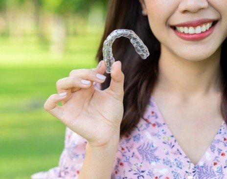 Smiling woman holding a clear aligner outdoors