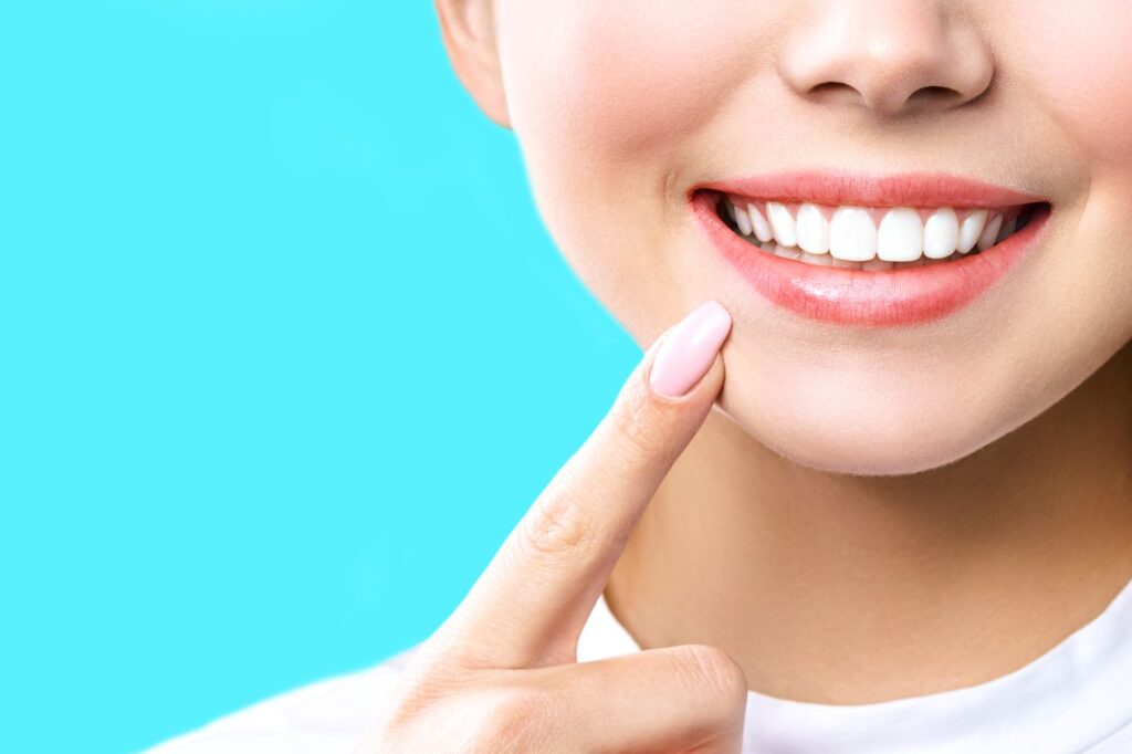 Nose-to-neck view of woman pointing to her white smile with bright blue background