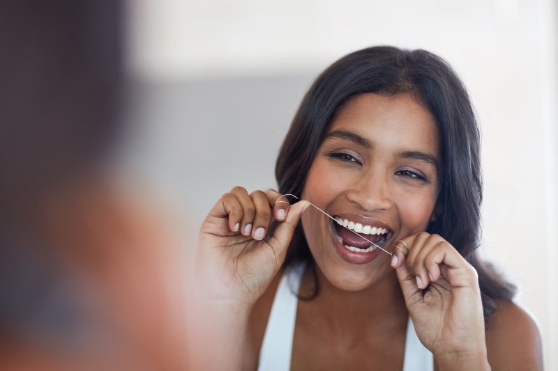 A woman flossing in front of a bathroom mirror